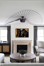 Load image into Gallery viewer, A beautifully arranged living room featuring the artwork titled 'Horse Art - Black Beauties 0230' prominently displayed above a fireplace. The art depicts two horses in a warm, natural setting, enhancing the elegant decor of the room with stylish furnishings and a contemporary chandelier.